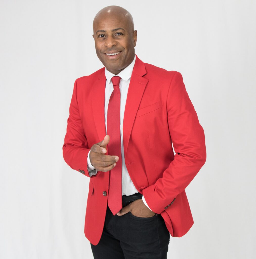 Julio Montalvo, trombonista cubano internacional, posando con chaqueta roja y corbata.